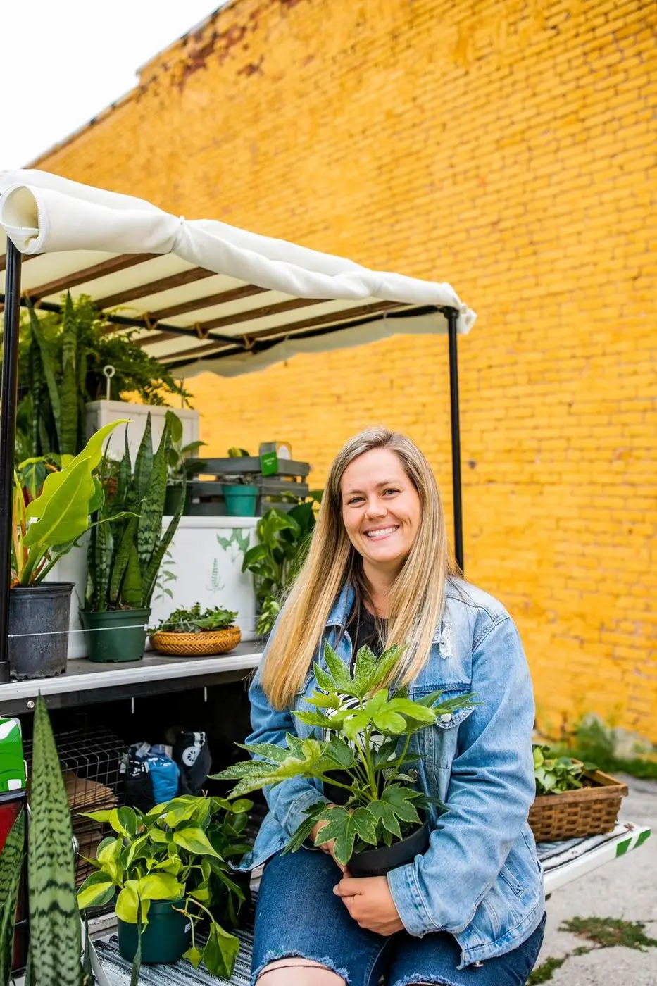 Tasha at the Mobile Joe tailgate with an armful of plants, against the yellow brick wall
